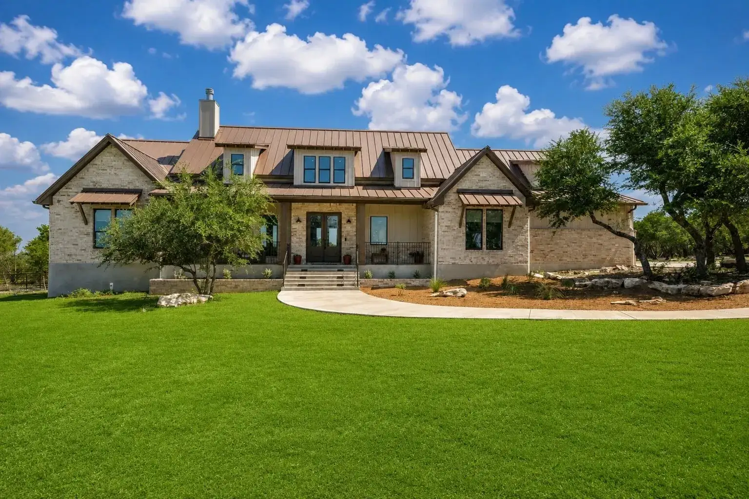 Stone and metal-roofed estate surrounded by green lawn and native trees